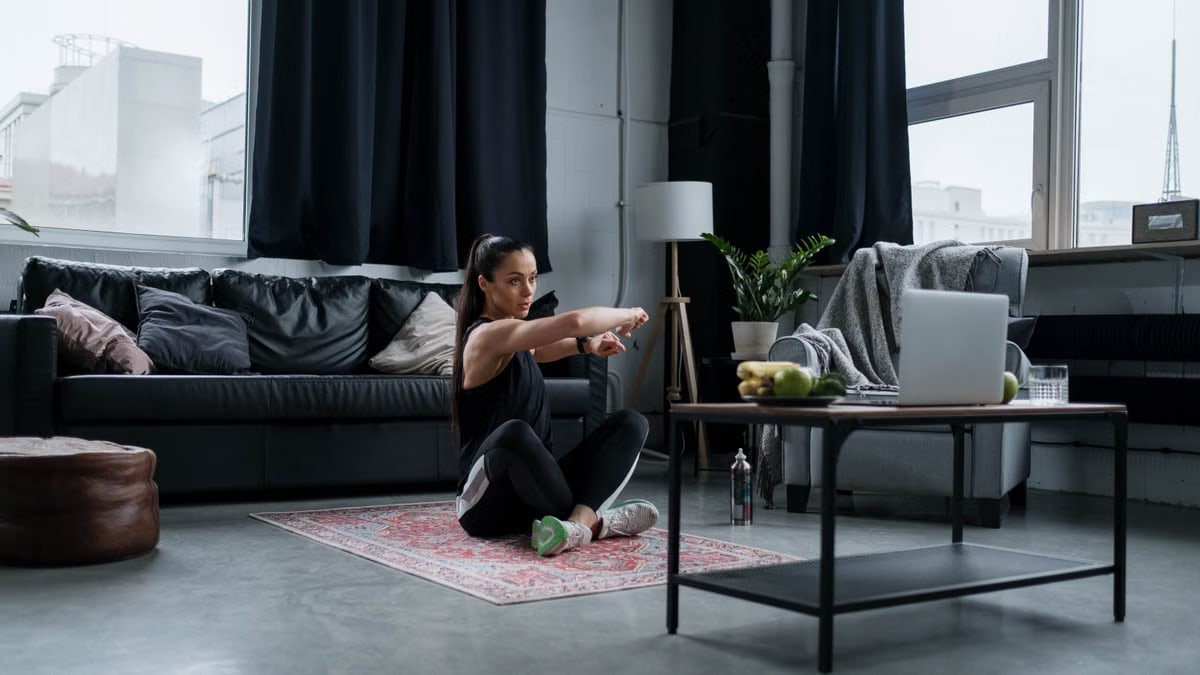 Woman doing exercise at home, sitting and stretching in a cozy living room.